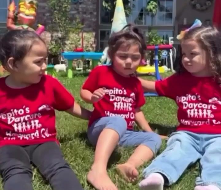 Three toddlers in red Pepito's Daycare shirts sitting together on the grass