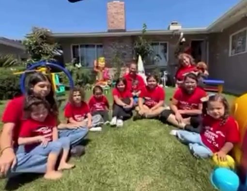 The whole group of kids in red Pepito’s Daycare shirts sitting on the lawn in front of the house